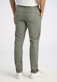Schmale graue Hosen aus strukturiertem Stoff, mit Gesäßtaschen und flacher Vorderseite. Kombiniert mit weißen Sneakers.