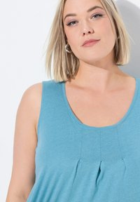 Top senza maniche azzurro chiaro con scollatura arrotondata, caratterizzato da sottili pieghe sul davanti e un tessuto morbido e testurizzato.