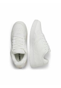 Ein Paar weiße Low-Top-Sneaker mit Schnürsenkeln, strukturierten Details und Perforationen an der Zehe, dargestellt in Vorderansicht und Seitenansicht auf einem weißen Hintergrund.