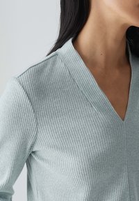 Ljusblå ribbad tröja med V-ringning. Tyget verkar mjukt med en texturerad yta, som visar vertikala linjer genom hela plagget.