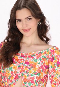 Blomstret bluse med livlige pink, orange og grønne mønstre. Den har en rund halsudskæring og let samlet effekt foran samt 3/4 ærmer.