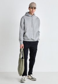 Grå hettegenser med kengurulomme, svarte cargo-bukser, beige caps, grønn totebag og hvite joggesko med svarte striper.