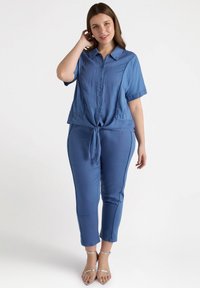 Completo due pezzi azzurro chiaro composto da una camicia a maniche corte con bottoni e legatura frontale, abbinata a pantaloni tapered con dettagli laterali.