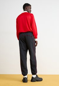 Rød langærmet skjorte med hvid krave, parret med sorte jogger-bukser med røde sidestriber og elastiske ankelmanchetter. Sorte klumpede sneakers.