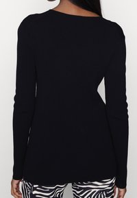 Schwarzer, gerippter Pullover mit langen Ärmeln, runder Halslinie und taillierter Silhouette, kombiniert mit gemusterten Schwarz-Weiß Leggings.