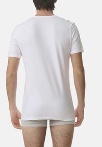 White short-sleeve T-shirt, soft cotton material, standard fit, round neckline, displayed from the back with gray shorts visible.