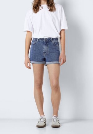 Jeansové šortky ve tmavě modré barvě s vysokým pasem a ohrnutými lemy. V kombinaci s volným bílým tričkem a šedými sportovními teniskami.