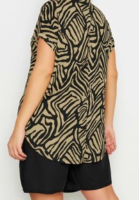 Top a maniche corte beige con un motivo astratto nero. Caratterizzato da un orlo arrotondato e un tessuto morbido e strutturato. Abbinato a pantaloni shorts neri.