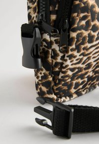 Kabelka s leopardím vzorom v čierno-hnedej farbe, vyrobená z odolného materiálu, ponúka dvojité zipsy a čierny popruh s nastaviteľnou sponou.