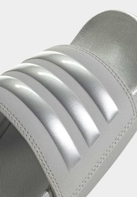 Sandal in grigio con una morbida fascia argentata lucida, caratterizzata da tre sezioni rialzate distinte, fodera interna testurizzata e cuciture resistenti.