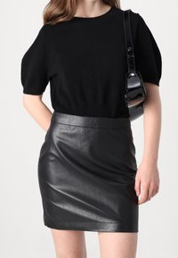 Svart stickad kortärmad topp med rundad halsringning, parat med en svart fusk-läder mini kjol. Kjolen har en slät yta och en åtsittande form.