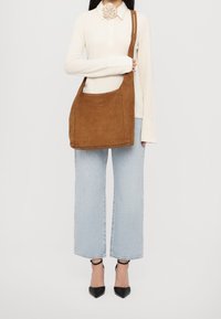 Brown suede shoulder bag with a single strap, rectangular shape, front pocket, soft texture, paired with light blue wide-leg jeans and black heels.