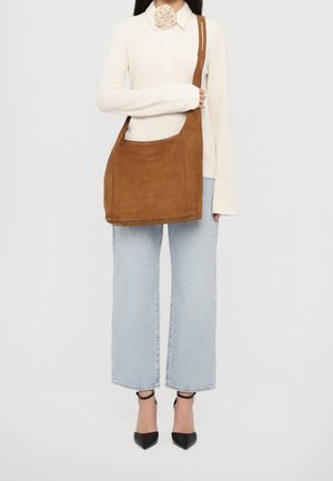 Brown suede shoulder bag with a single strap, rectangular shape, front pocket, soft texture, paired with light blue wide-leg jeans and black heels.