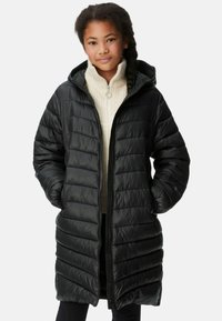 Cappotto lungo imbottito nero con cappuccio, caratterizzato da trapuntature orizzontali, una zip completa e due tasche laterali. Indossato sopra un maglione color crema.