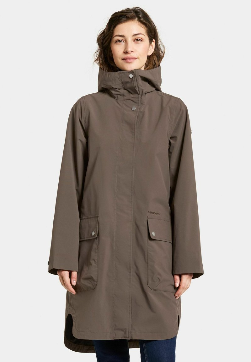 Tumma ruskea vedenpitävä takki, jossa on korkea kaulus, edessä napitettu sulku ja kaksi suurta taskua. Ominaisuuksiin kuuluu rento istuvuus ja pitkät hihat.