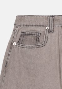 Gray denim fabric showcasing a close-up of the waistband, featuring a small pocket, silver hardware, and contrasting stitching details.