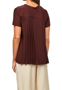 Haut bordeaux à manches courtes avec un détail plissé dans le dos, texture lisse, encolure ronde et ourlet net, associé à un pantalon couleur crème.