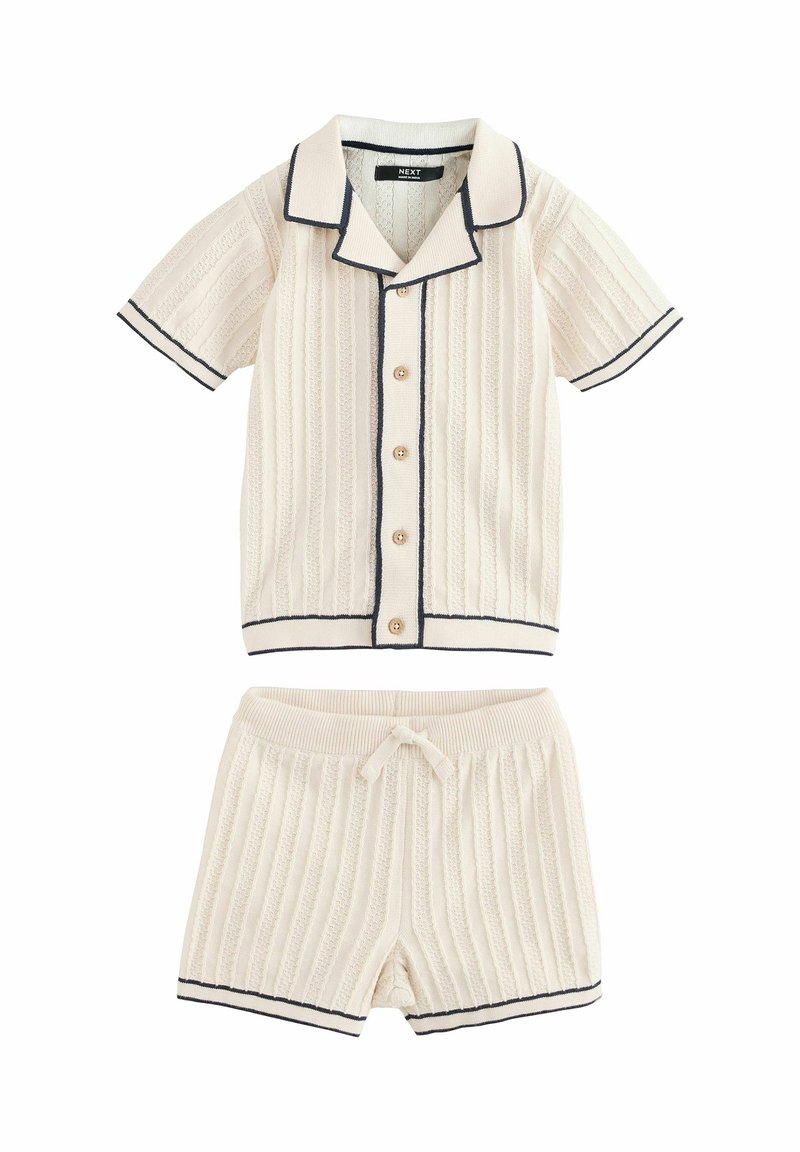 Pyjamasæt i cremefarvet ribbet stof med marineblå kant. Kortærmet skjorte med knapper og shorts med elastisk talje og snor.