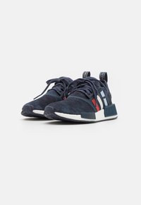 Sportovní tenisky námořnicky modré barvy s vrchní částí z broušené kůže, s bílými a červenými pruhy, kulatými tkaničkami a texturovanými gumovými podešvemi.