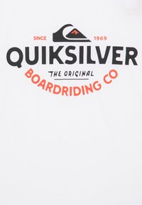 Bílá bavlněná tričko s výrazným černým a oranžovým textem s názvem značky "Quiksilver", logem a sloganem "Boardriding Co".
