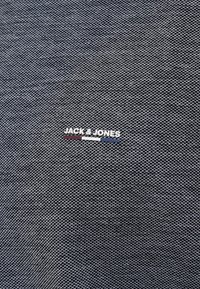 Tamsiai mėlynas audinys su matomu Jack & Jones logotipu, turinčiu baltą užrašą ir spalvinius akcentus raudonos ir mėlynos spalvos.