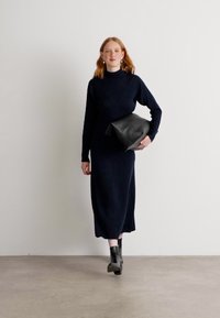 Vestido de punto de manga larga en color azul marino, con un cuello alto y un corte relajado, acompañado de un bolso de mano negro y botines de tacón alto.