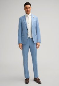 Helles blaues Anzug mit taillierter Passform, strukturiertem Stoff, einreihigem Sakko, weißer Weste und braunen klassischen Schuhen. Akzentblume an der Revers.