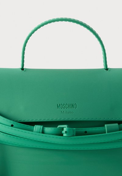 Πράσινη τσάντα Moschino Milano με χειρολαβή και ρυθμιζόμενο ιμάντα σε κοντινή λήψη.
