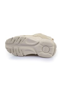 Beige athletic shoe sole features a textured rubber material with a ridged pattern for traction, and a circular logo imprint in the center.