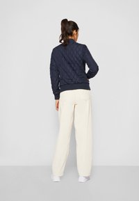 Navy quilted bomber jacket with ribbed cuffs and hem, paired with cream wide-leg pants and white sneakers, viewed from the back.