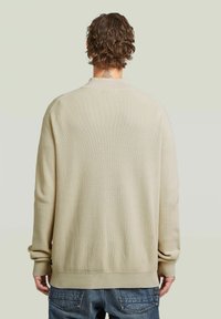 Lichtbeige gebreide trui met ribbeltextuur, lange mouwen en een ronde halslijn, met een ontspannen pasvorm en zonder zichtbare versieringen.