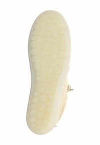 Suola di una scarpa beige con un motivo circolare testurizzato. La gomma è liscia e flessibile con un colore chiaro. Lacci e dettagli in metallo visibili.