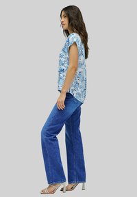 Top blu con motivo floreale e maniche corte, abbinato a jeans blu a vita alta e gamba larga, e tacchi con cinturini beige.
