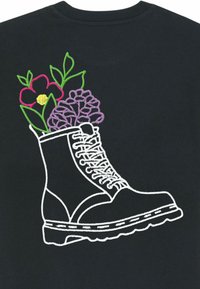 Zwarte t-shirt met witte borduursels van een laars gevuld met kleurrijke bloemen en groene bladeren, waarbij de veters en details van de zool van de laars worden benadrukt.