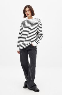 Chemise à rayures noires et blanches à manches longues avec un col rond, associée à un jean large gris foncé et des chaussures noires.