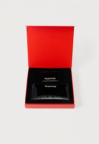Conjunto de carteira de couro patente preta e porta-cartões dentro de uma caixa vermelha. Ambos os itens apresentam a marca em dourado "Valentino". Textura suave, design elegante.