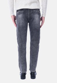 Jeans in denim grigio a taglio slim, con una texture sbiadita, due tasche posteriori e vita bassa, abbinati a scarpe nere.