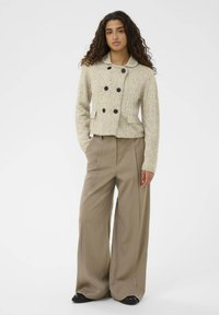 Bež pleteni kratki kaput s dvostrukim gumbima, crnim dugmadi i dva prednja džepa, uparen s hlačama širokih nogavica u taupe boji.