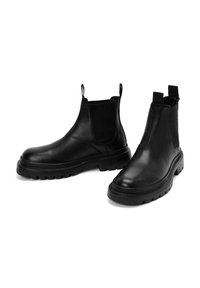 Bottes Chelsea en cuir noir avec côtés élastiques, semelle en caoutchouc épaisse et languettes à l'arrière. Texture lisse avec un design à bout arrondi.