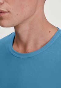 Light blue crew neck t-shirt featuring a smooth texture and short sleeves, with a close-up view of the neckline and collar detail.