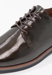Chaussure habillée en cuir marron avec une texture brillante et côtelée, dotée de lacets marron et d'une semelle foncée contrastée. Coutures détaillées le long des bords.