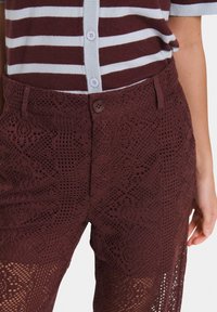 Pantaloni in pizzo borgogna con un motivo testurizzato a maglia aperta, dotati di chiusura con bottone e tasche laterali. Indossati con una maglietta a righe.