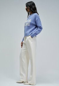 Jasnoniebieski sweter z dzianiny z napisem "USA JEANS", zestawiony z białymi spodniami o szerokich nogawkach i kremowymi czółenkami. Minimalistyczny design.