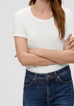 Haut blanc texturé à manches courtes avec un col rond, associé à un jean taille haute en denim foncé avec des coutures visibles et des poches avant.