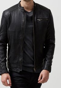 Svart läderjacka med en åtsittande krage, framzipper och en liten dragkedjeficka på bröstet. Lätt sliten textur, minimal detaljering.