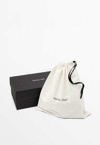 Boîte rectangulaire noire et pochette en tissu blanche à cordon avec logo "Massimo Dutti" sur fond blanc.