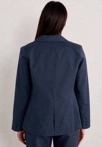 Navy blazer made of structured fabric, featuring a notched collar, three-button cuffs, and a vent at the back. Smooth texture.