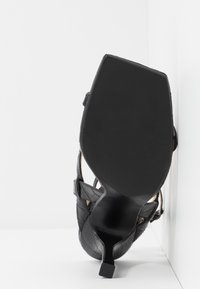 Musta korkokenkä, jossa on nelikulmainen varvas, texturoitu nahkapinta ja sileä musta pohja, varustettu nilkkahihnoilla tukemaan jalkoja.