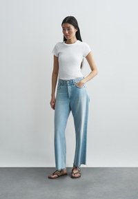 Vaaleansiniset farkut leveällä lahkeella ja frayed-helmillä, yhdistettynä istuvaan valkoiseen lyhythihaiseen t-paitaan ja ruskeisiin sandaaleihin.