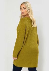 Olivenfärgad oversized stickad tröja med avslappnad passform, ribbade ärmslut och nederkant, som visar en strukturerad textur och en V-ringad design.